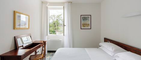 Habitación de hotel con cama, escritorio con silla, ventana con cortinas y dos cuadros en las paredes.
