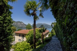 Un sentiero conduce a un edificio con tetto rosso, immerso nel verde e con una montagna sullo sfondo.
