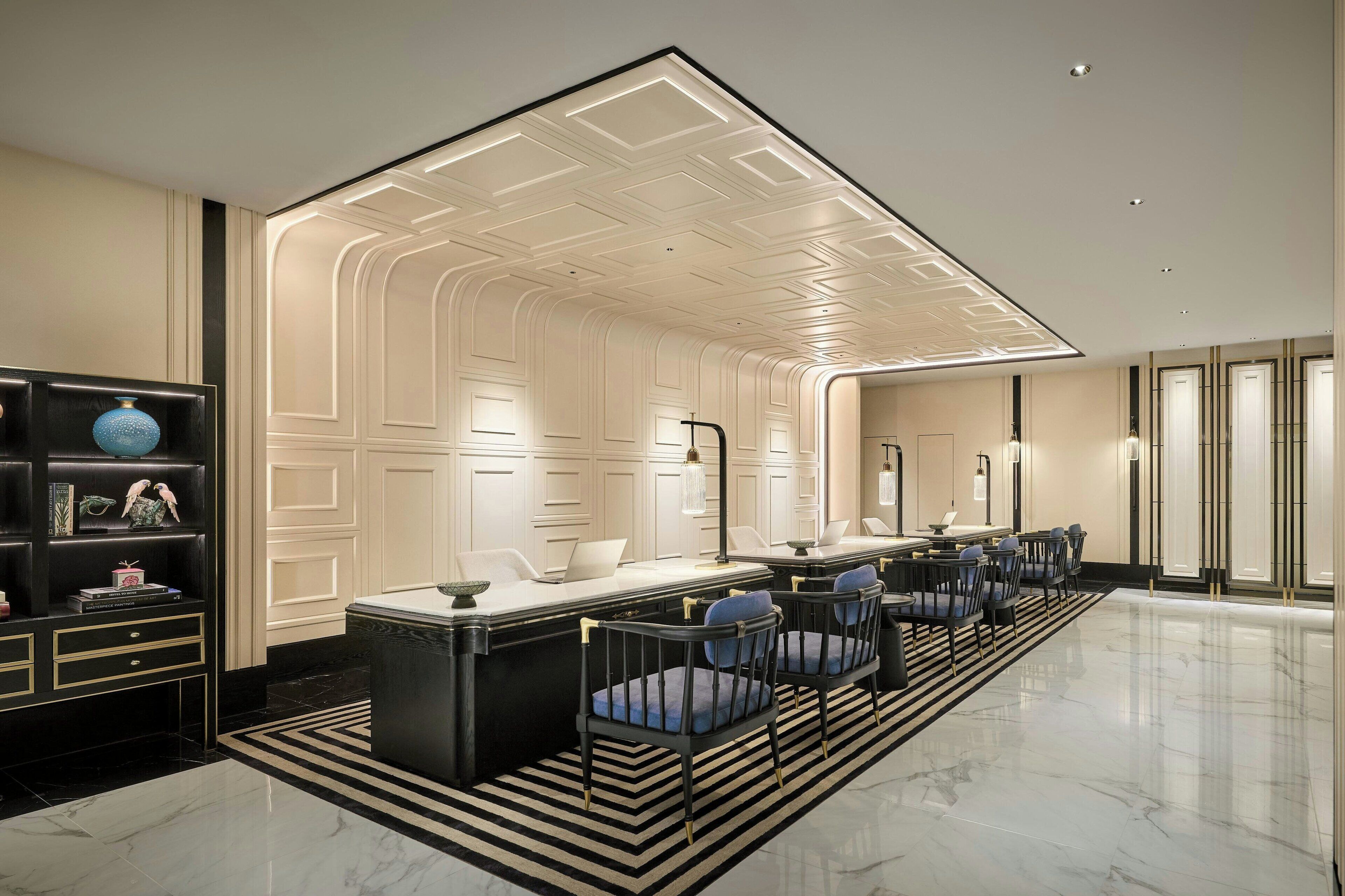 Um lobby moderno de hotel com um balcão de recepção central, área de estar e uma estante decorativa.
