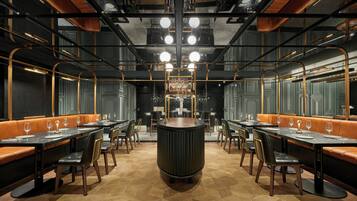 Un restaurant avec de hauts plafonds, des conduits apparents et une grande table ronde au centre, entourée de banquettes et de tables à manger.