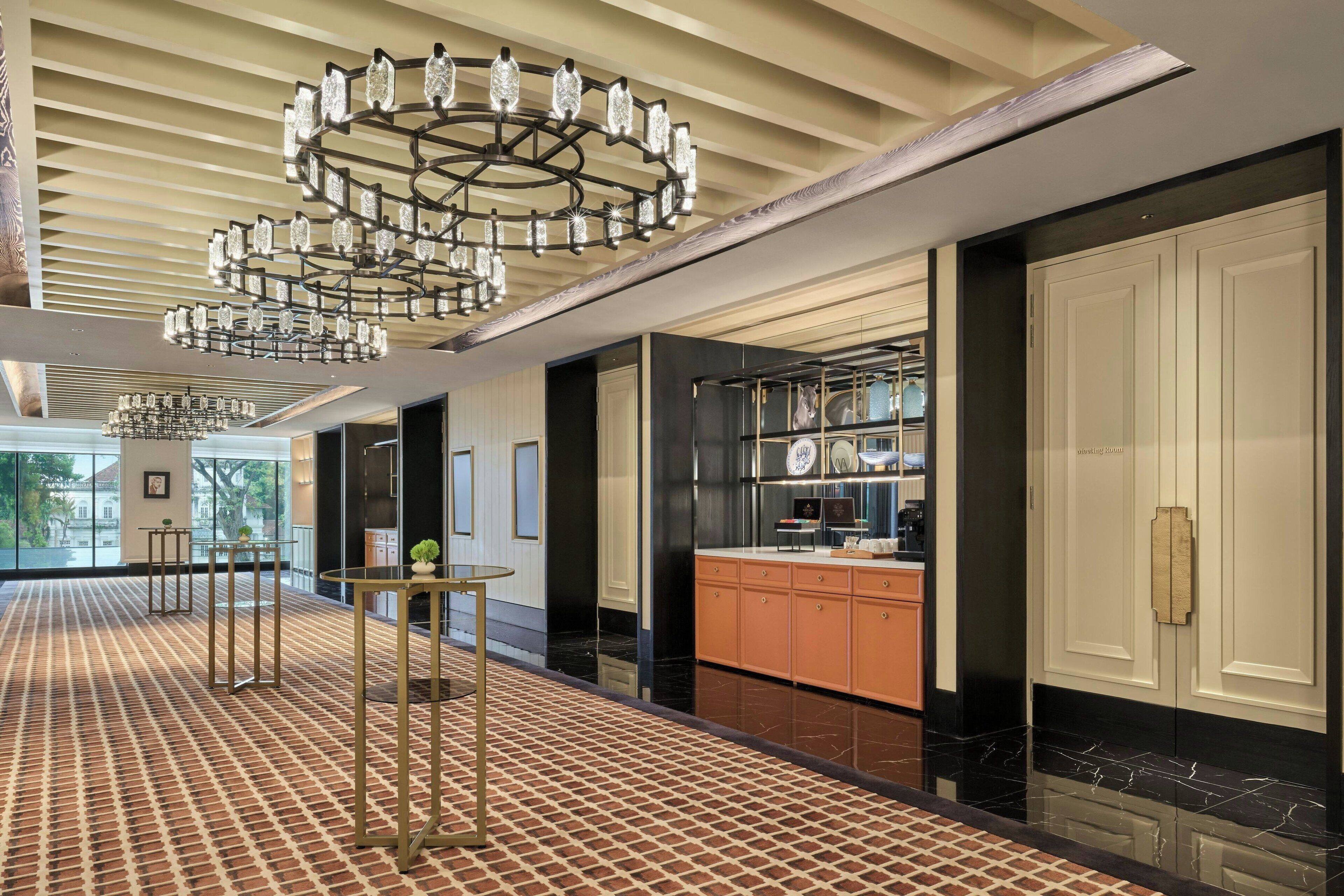 Un hall d’entrée spacieux, doté d’un tapis à motifs, d’un lustre central et d’un coin cuisine avec des placards et un plan de travail.