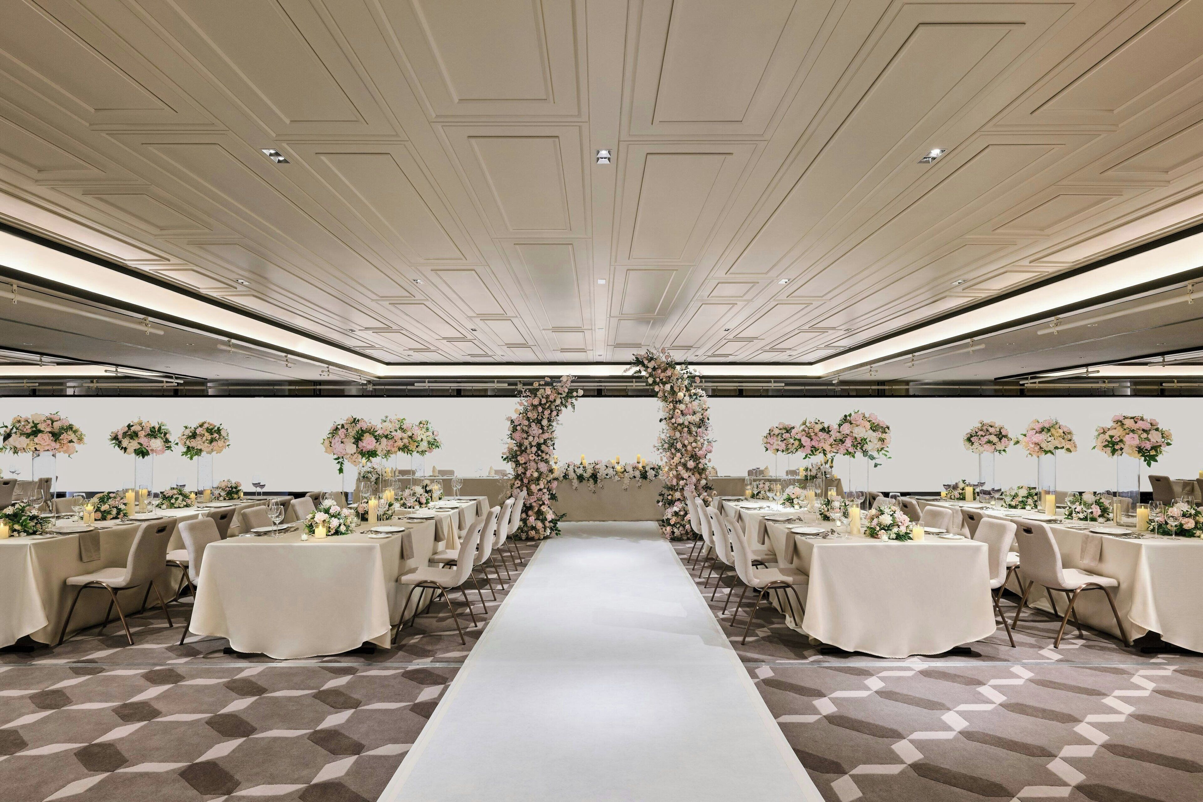Un salón de banquetes con un pasillo central, mesas a ambos lados y arreglos florales en las paredes.