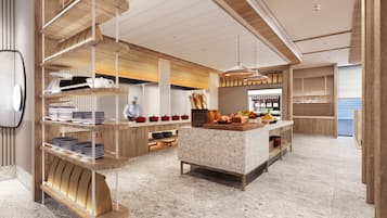 Une cuisine moderne avec des meubles en bois, un îlot central agrémenté de fruits et de pain, et un chef qui prépare les plats.