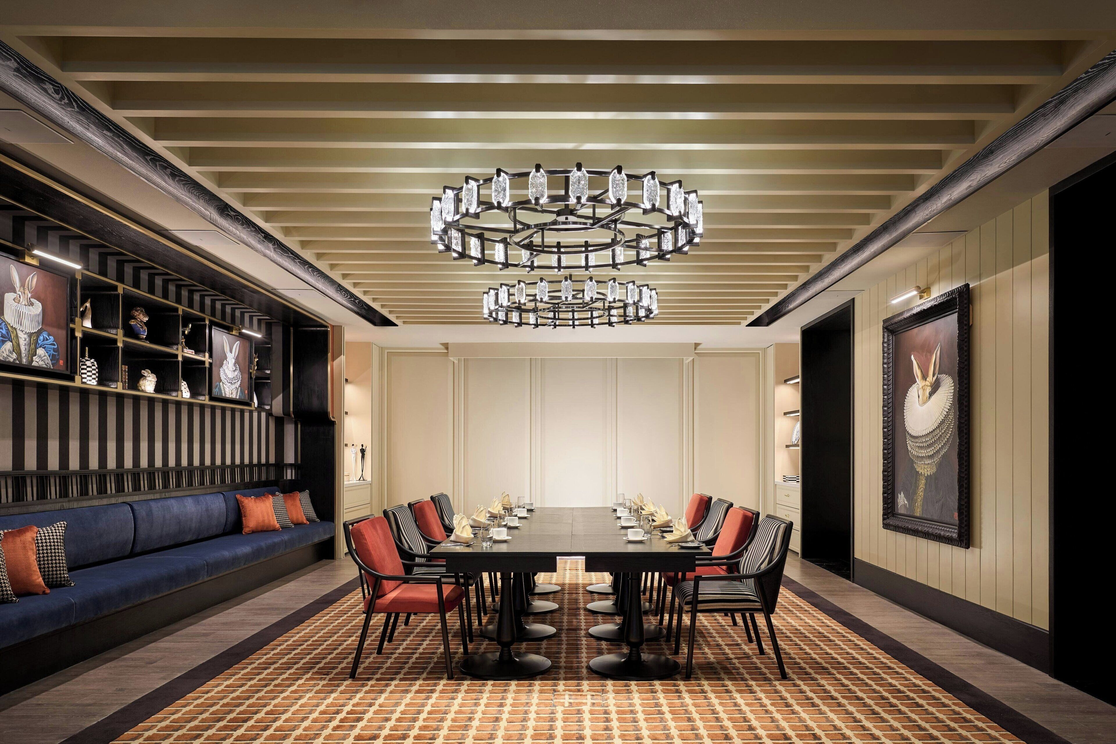 A conference room with a long table, chairs, a chandelier, a sofa, and shelves with decorative items.