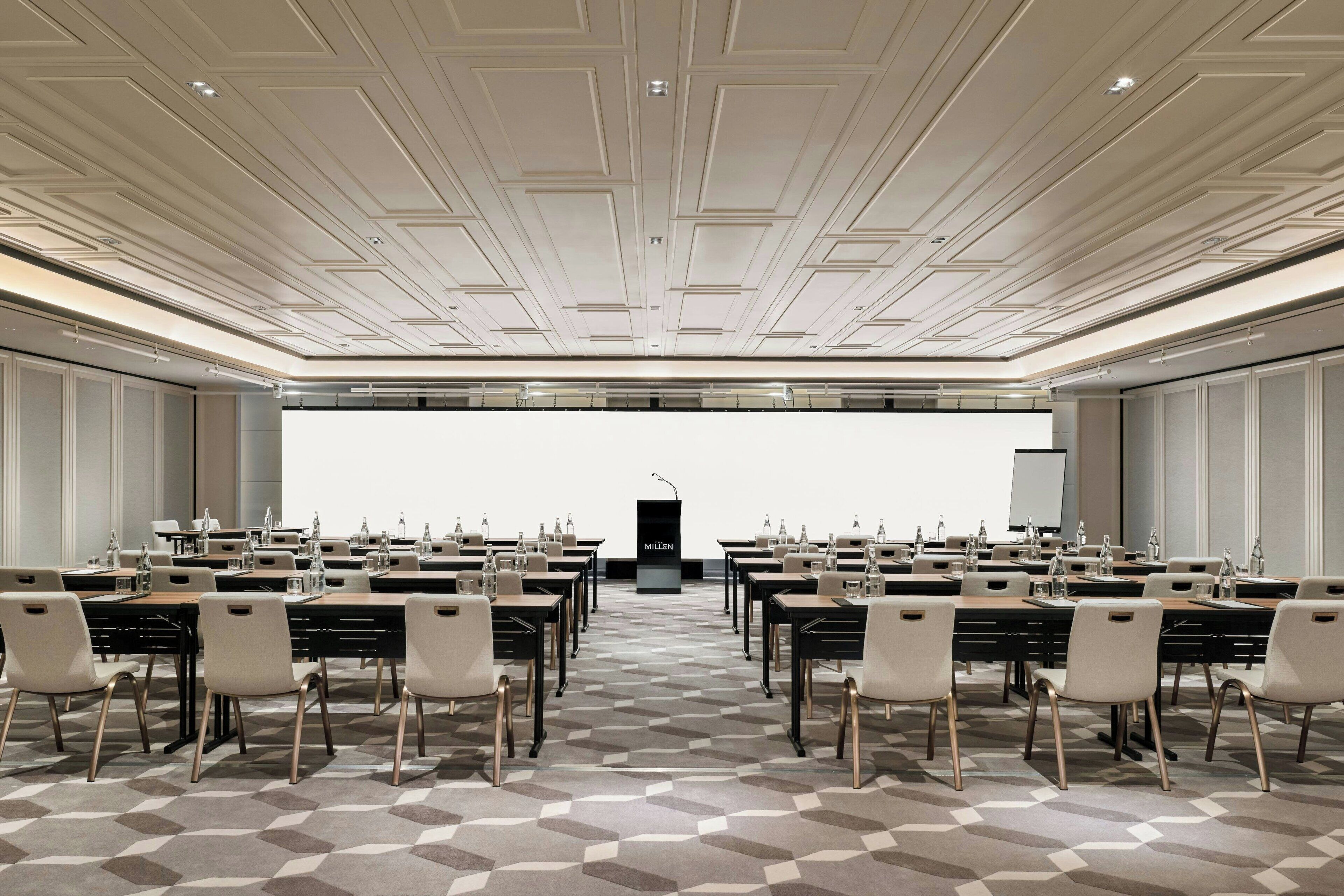 A conference room with a podium, tables, chairs, and a projector screen.