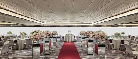 Un salón de banquetes con alfombra roja, mesas adornadas con centros de flores y un suelo de diseño geométrico.