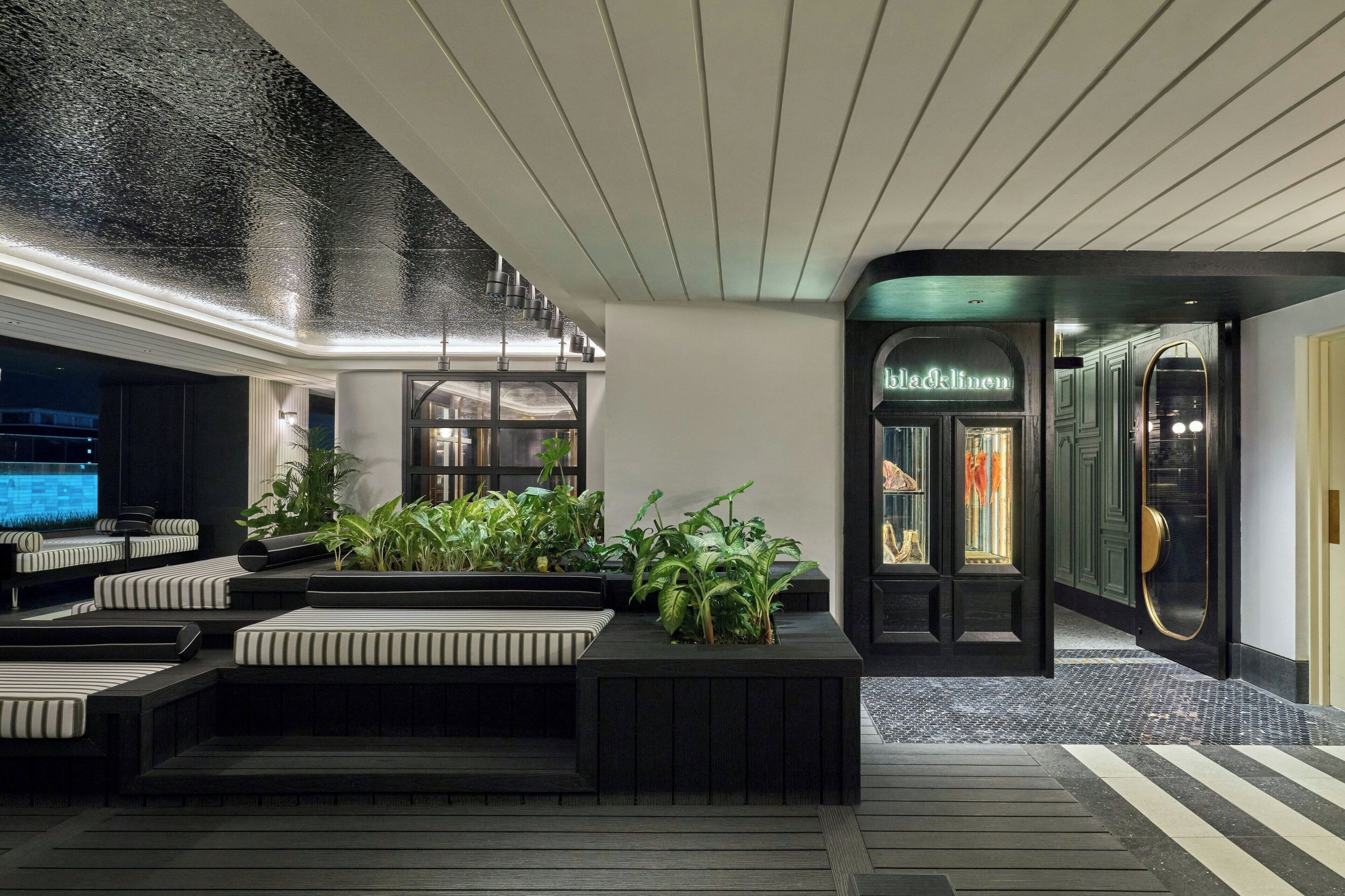 Een moderne lobby met een zithoek, een televisie en een winkel genaamd 'Black Linen'.