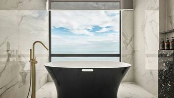 A modern bathroom with a freestanding bathtub, a gold showerhead, and a view of the sky through a large window.