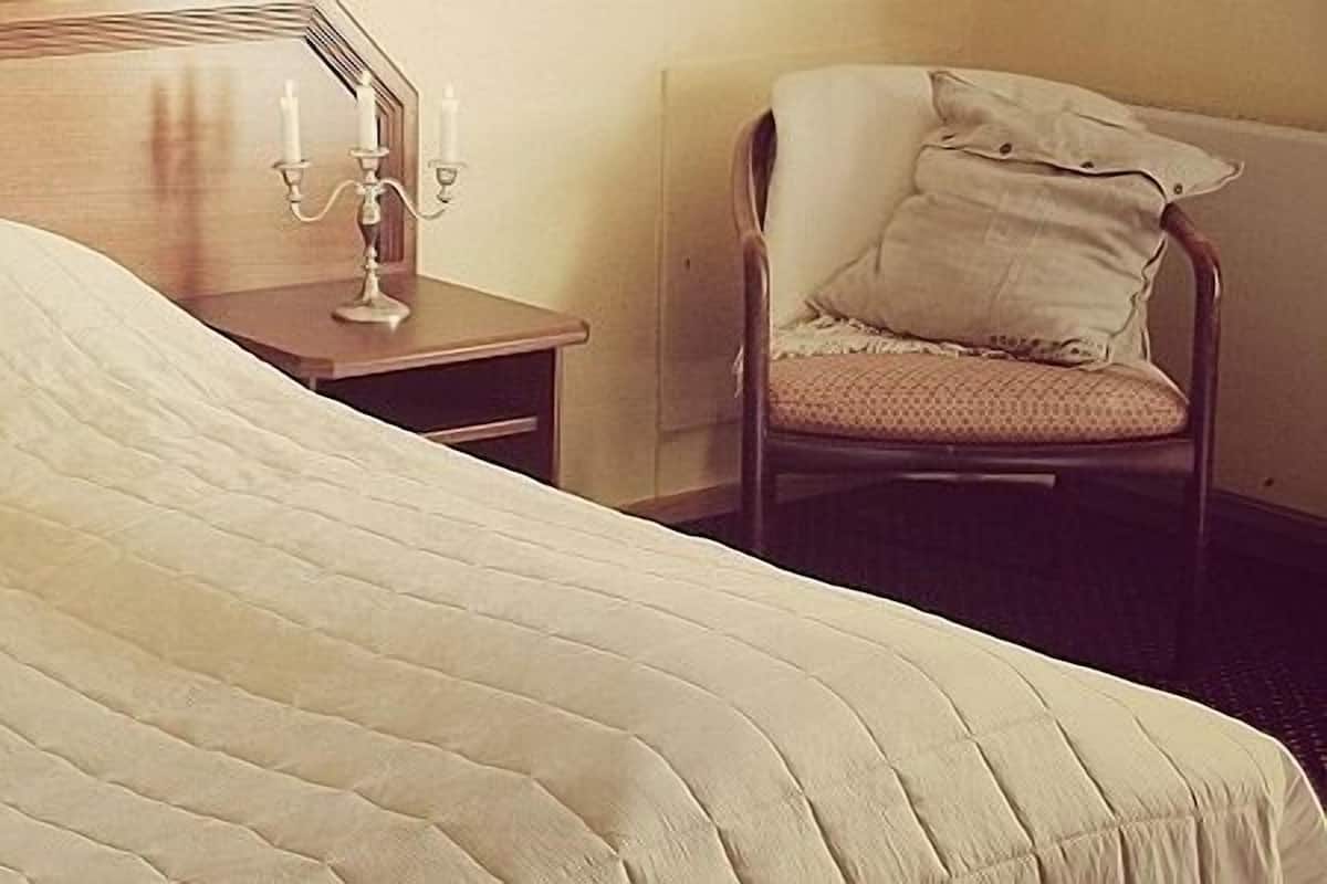 A bed with a quilted cover, a wooden headboard, and a nightstand with a candelabra.