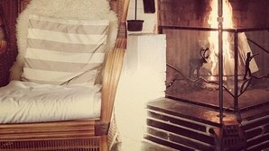A room with a wooden chair, a fireplace with a metal grate, and a staircase leading to an upper level. - Dovrefjell Hotell (Dovre)