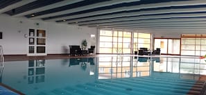 An indoor swimming pool with clear blue water, surrounded by windows and a ceiling with blue and white stripes. - Dovrefjell Hotell (Dovre)