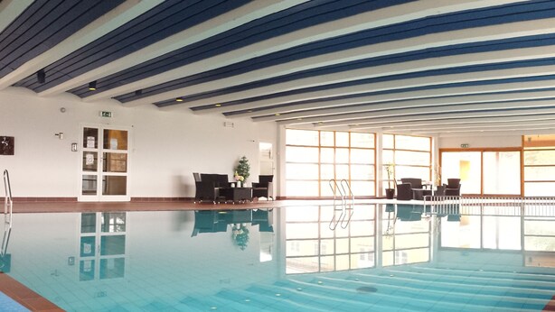An indoor swimming pool with clear water, a tiled floor, and a ceiling with blue and white beams. - Dovrefjell Hotell (Dovre)