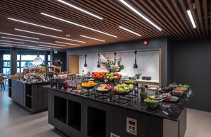 A modern kitchen area with a buffet setup featuring various fruits, vegetables, and condiments.