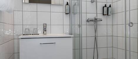 A modern bathroom with a glass-enclosed shower, white tiles, a vanity with drawers, and a toilet.