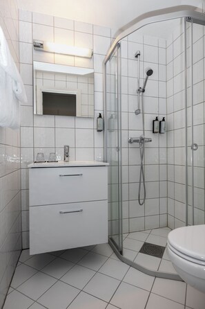 A modern bathroom with a glass-enclosed shower, white tiles, a vanity with drawers, and a toilet.