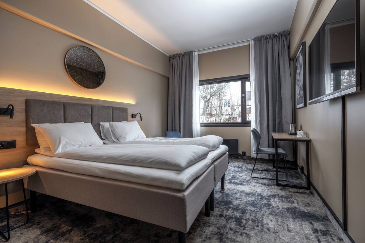 A modern hotel room with a large bed, a desk, and a chair.
