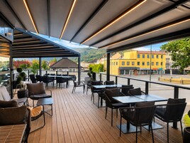 Un patio al aire libre con mesas y sillas, un área de estar techada y vistas a edificios y montañas.