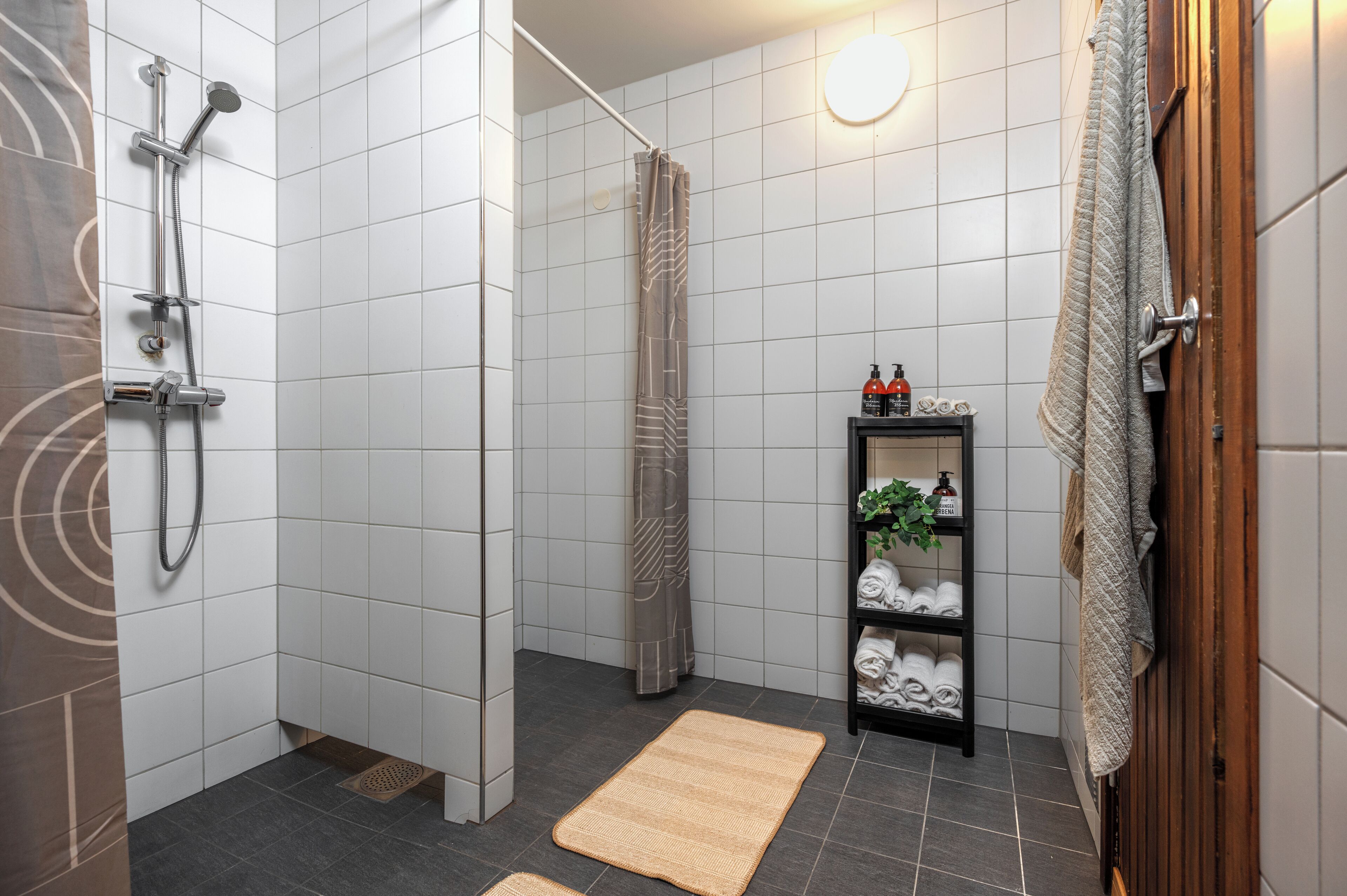 A modern bathroom with a shower, a towel rack, a shelf with toiletries, and a mat on the floor.