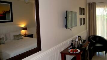A hotel room with a bed, a desk with a plate of strawberries, a chair, a TV, and a ceiling fan.
