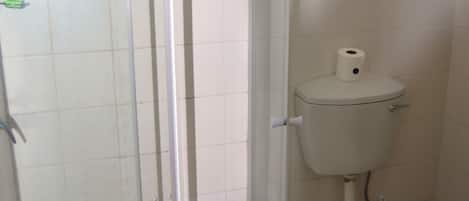 Un baño con inodoro, cabina de ducha y dispensador de papel higiénico.