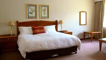 A neatly made bed with white linens, two bedside tables with lamps, and two framed botanical prints on the wall.