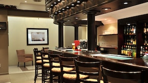 A bar area with a long counter, multiple chairs, a coffee machine, and a well-stocked liquor shelf. - Safari Hotel & Convention Centre (Rustenburg)