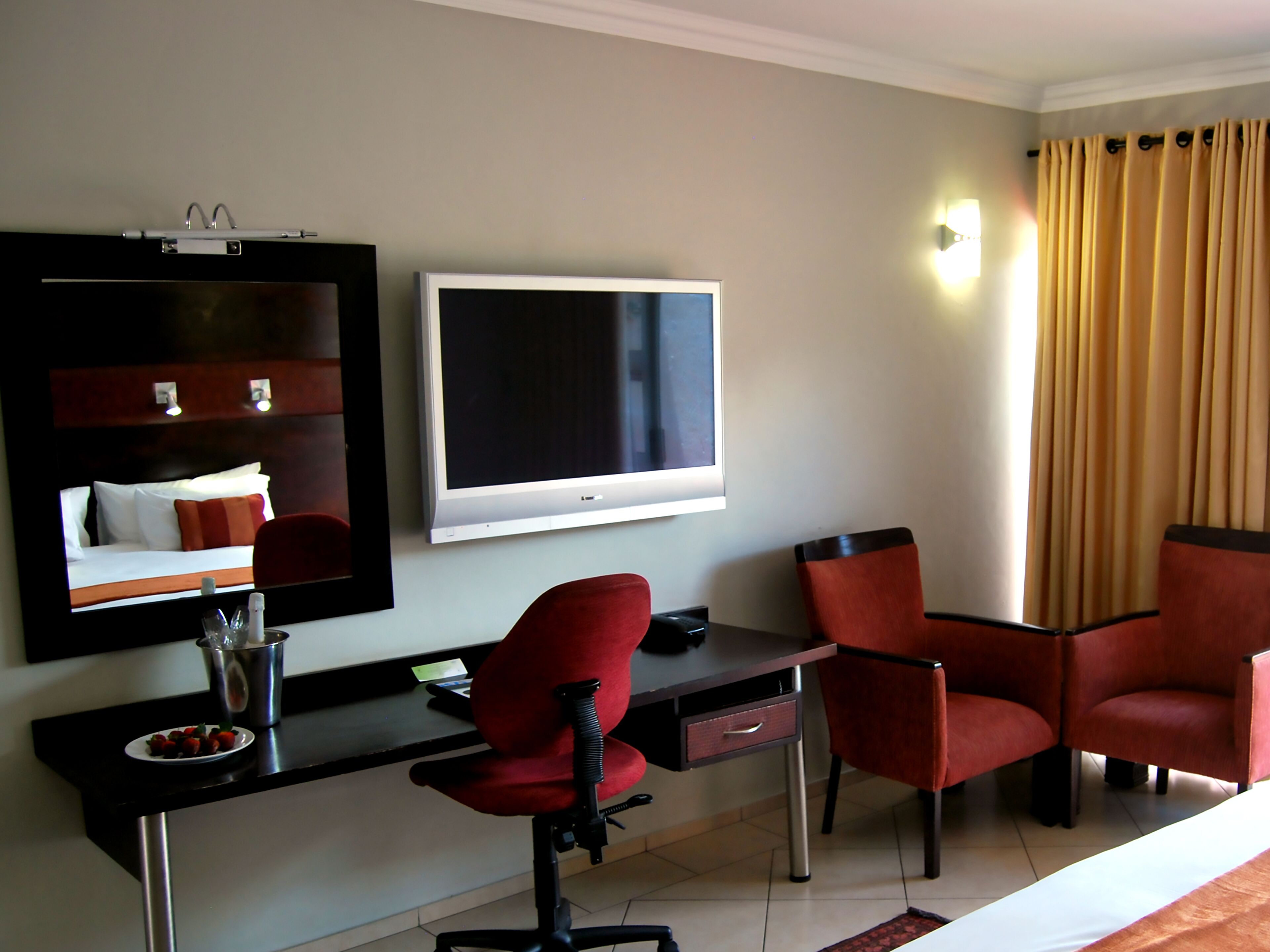 Quarto de hotel com uma cama, uma escrivaninha com cadeira, uma televisão e um espelho grande.
