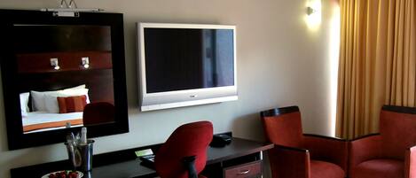 A hotel room with a bed, a desk with a chair, a television, and a large mirror.
