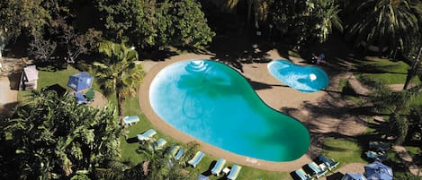 An aerial view of a resort with two large swimming pools surrounded by palm trees and lounge chairs.