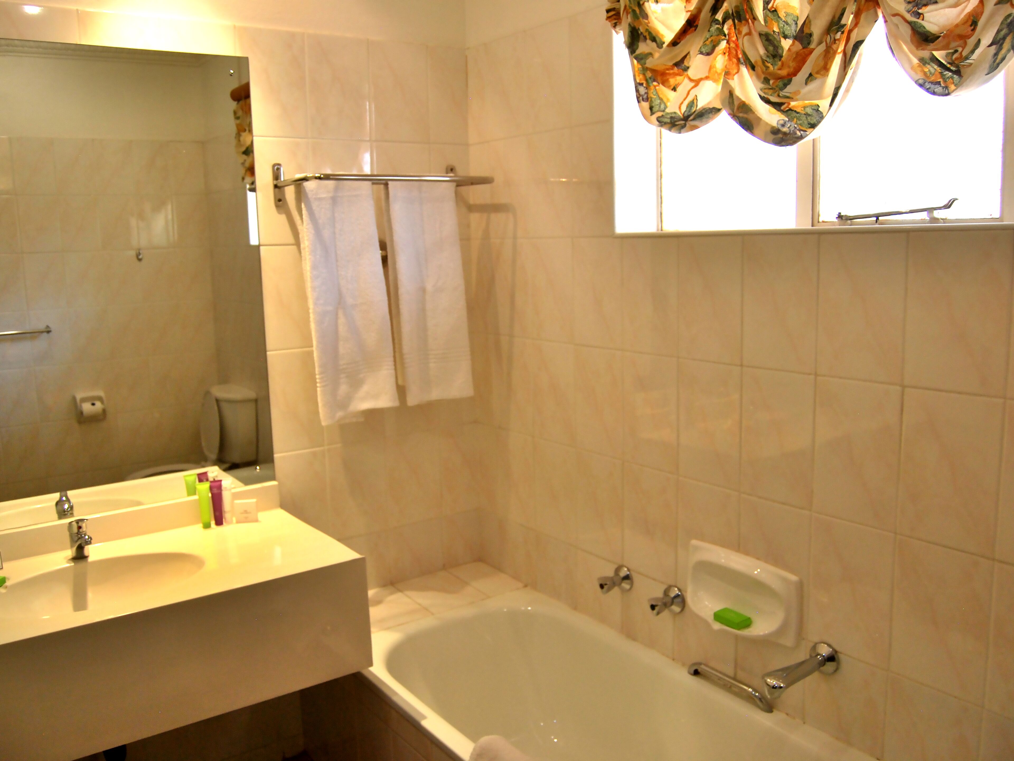 A bathroom with a bathtub, a sink, a mirror, a towel rack, and a window with curtains.