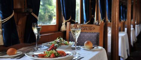 A dining table set with plates of food, a glass of white wine, and a small bread roll.