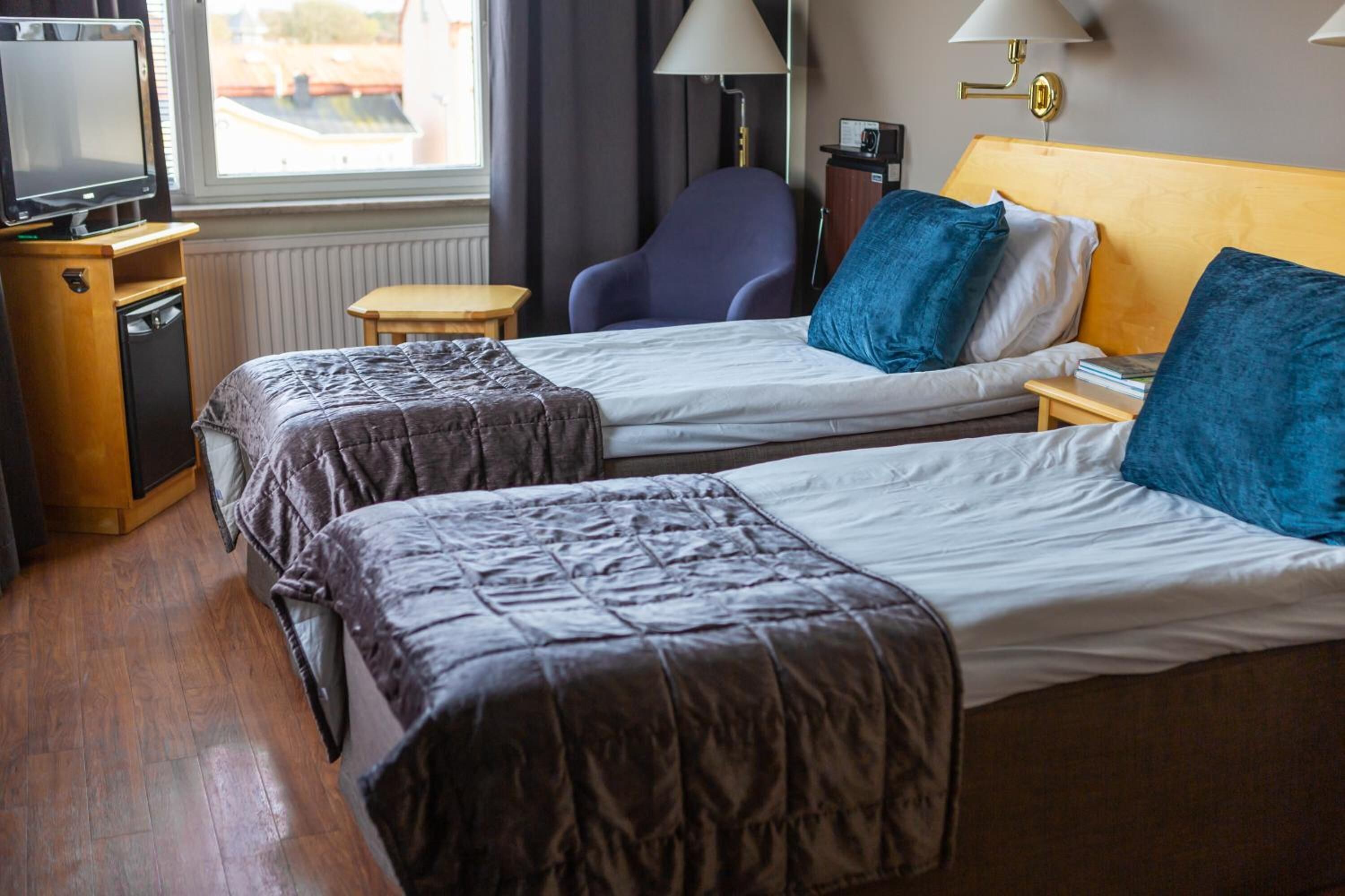 A hotel room with two beds, a television, a lamp, and a chair.