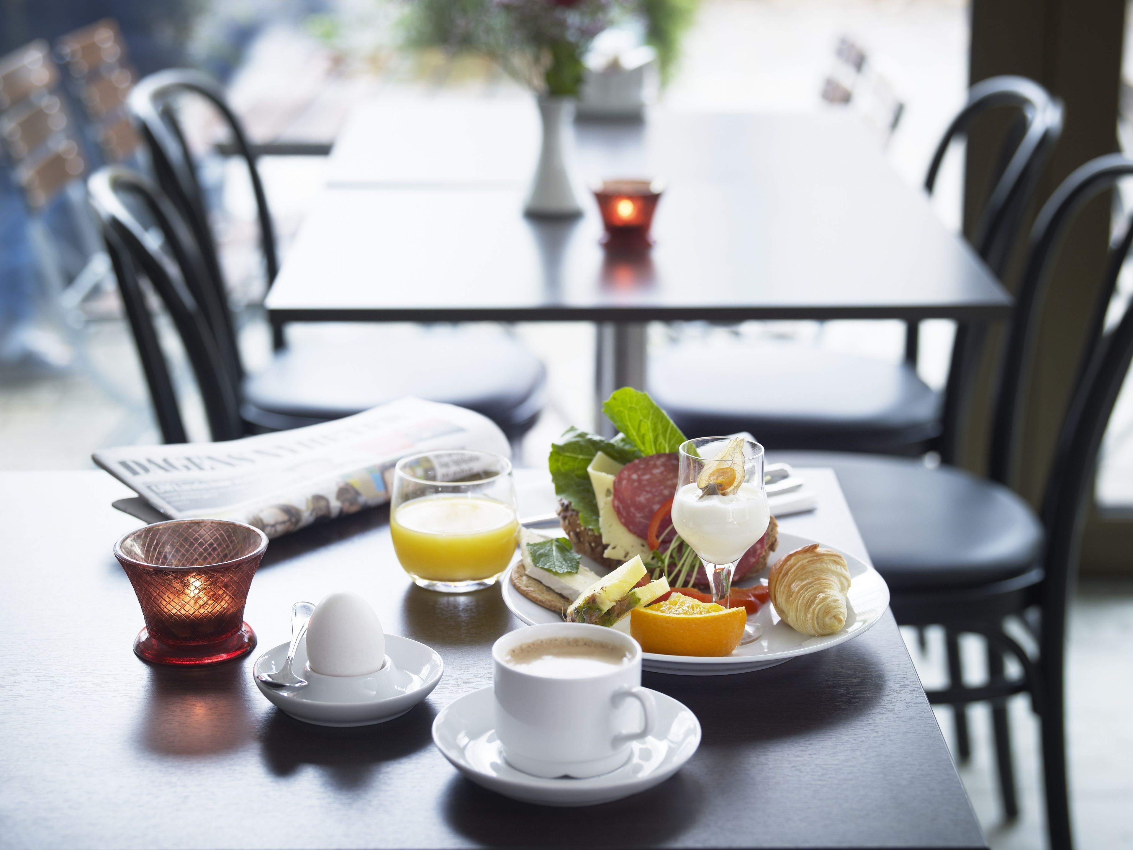 A dining table with a croissant, a glass of orange juice, a cup of coffee, and a plate of food including cheese, tomato, and leafy greens.