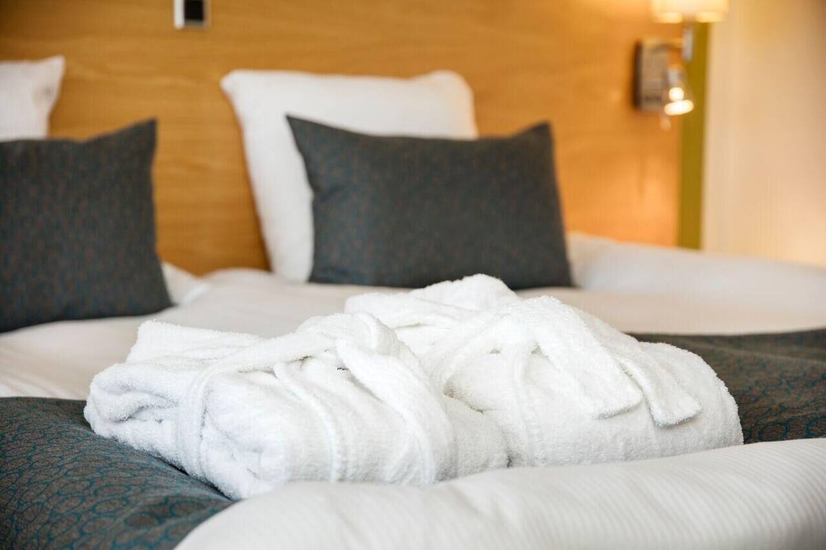 A neatly made bed with white bedding and a rolled white towel on the side.