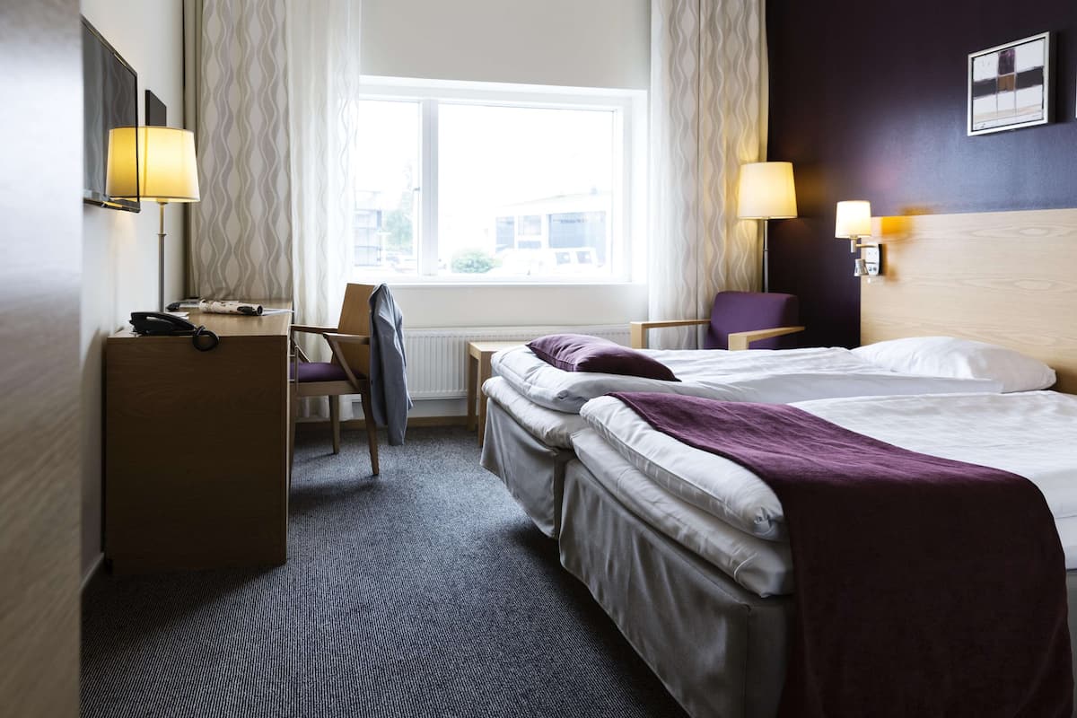 A hotel room with a bed, a desk, a chair, and a window.