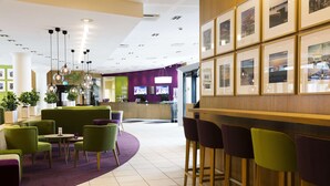 A modern hotel lobby with a reception desk, green and purple seating, and a bar area. - Scandic Aalborg City (Aalborg)