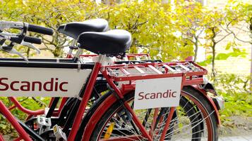 Una bicicleta vermella amb un cistell i dos seients, aparcada davant d'un edifici amb un rètol que diu "Scandic".