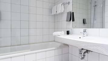 A modern bathroom with white tiles, a bathtub, a sink, and a glass-enclosed shower.