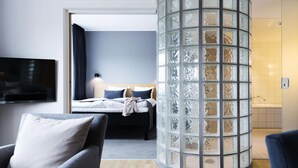 A hotel room with a bed, a TV, a glass partition, and a bathroom with a bathtub. - Scandic Aalborg City (Aalborg)