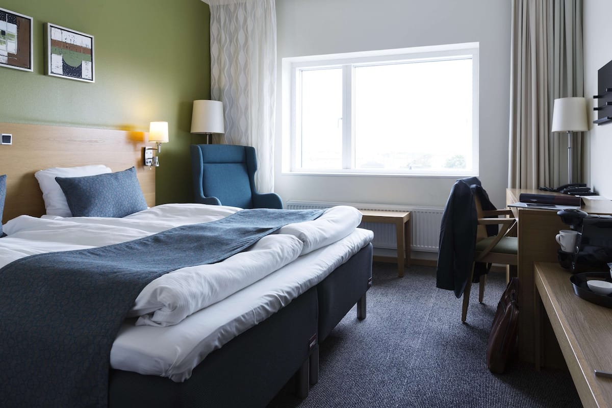 A hotel room with a large bed, a desk, a chair, and a window with curtains.