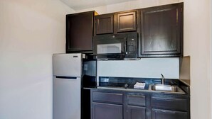 A compact kitchen with dark cabinets, a white refrigerator, a microwave, and a sink. - Studio 6 Extended Stay - Ocean Springs, MS (Ocean Springs)