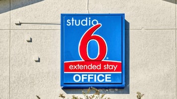 Un panneau bleu avec l’inscription « studio 6, location de bureaux pour séjours prolongés » est fixé au mur d’un immeuble.