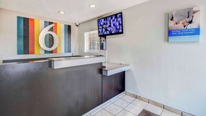A reception area with a large number '6' sign, a flat-screen TV, and a poster advertising budget extension. - Studio 6 Extended Stay - Ocean Springs, MS (Ocean Springs)