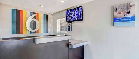 A reception area with a large number '6' sign, a flat-screen TV, and a poster advertising budget extension.