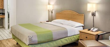 A hotel room with a bed, bedside table, lamp, and a small wooden bench.