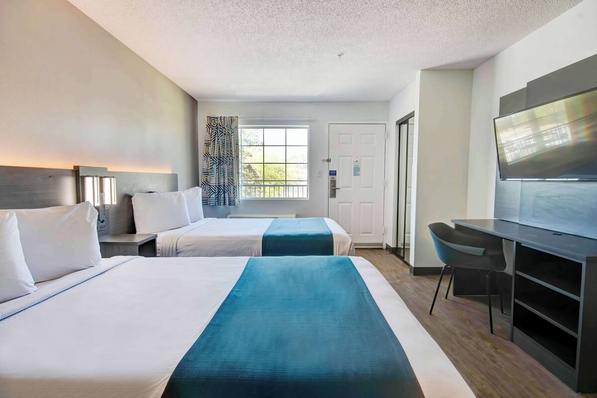 Habitación de hotel con dos camas, un escritorio, una silla, un televisor y una ventana con cortinas.