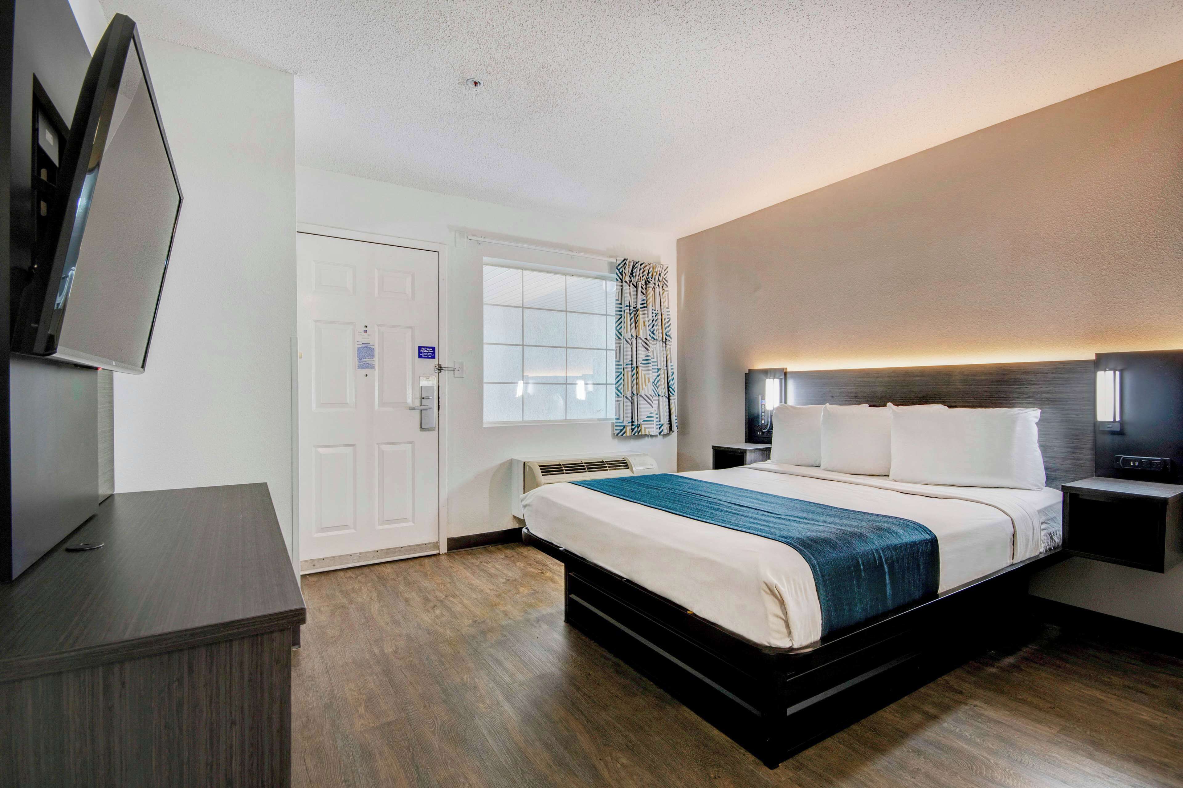 A hotel room with a bed, bedside tables, a TV, and a window with curtains.