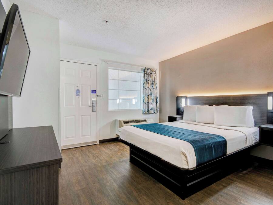 A hotel room with a bed, bedside tables, a TV, and a window with curtains.