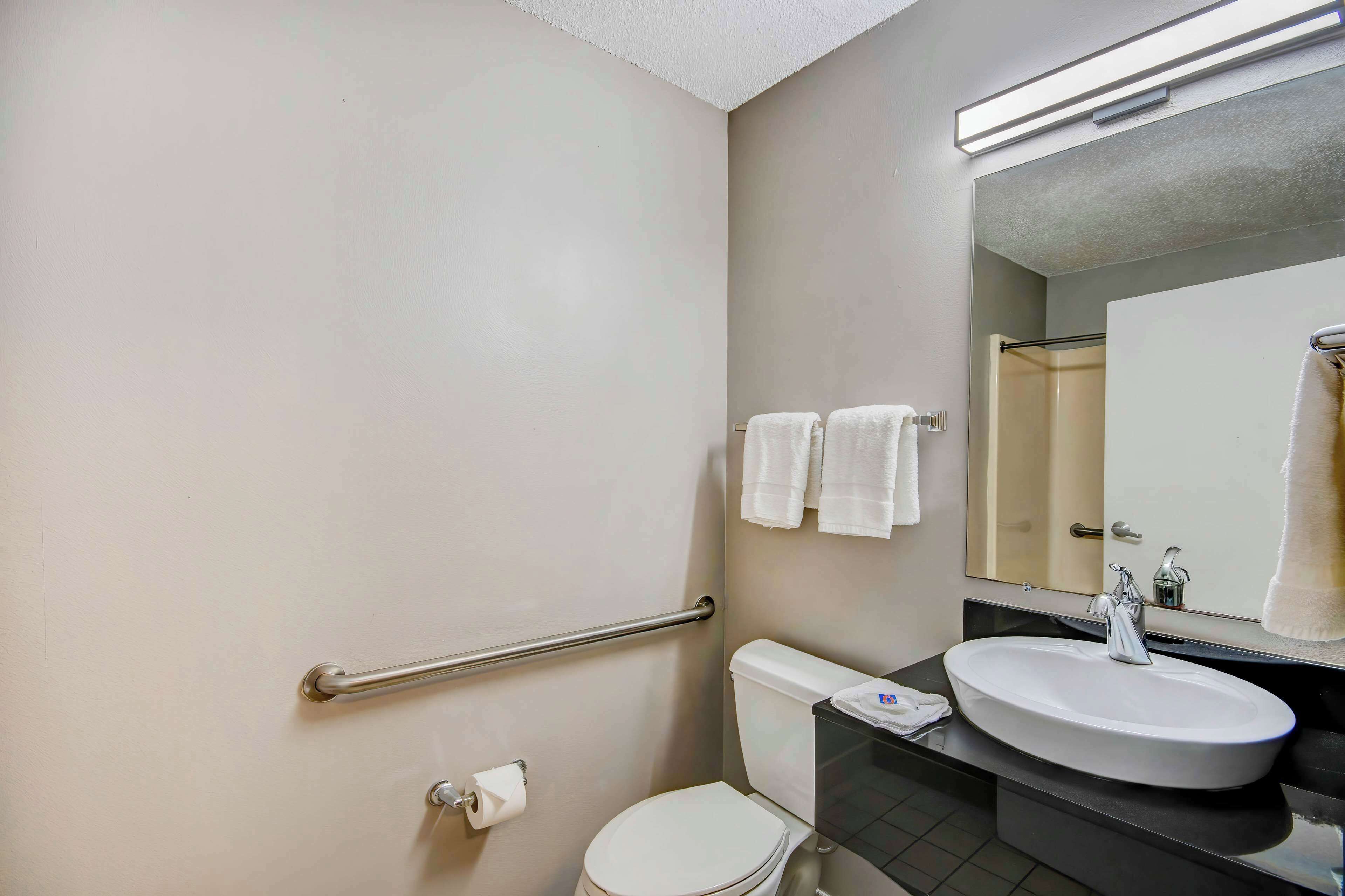 Un baño con un inodoro blanco, un lavabo con espejo y un pasamanos en la pared.