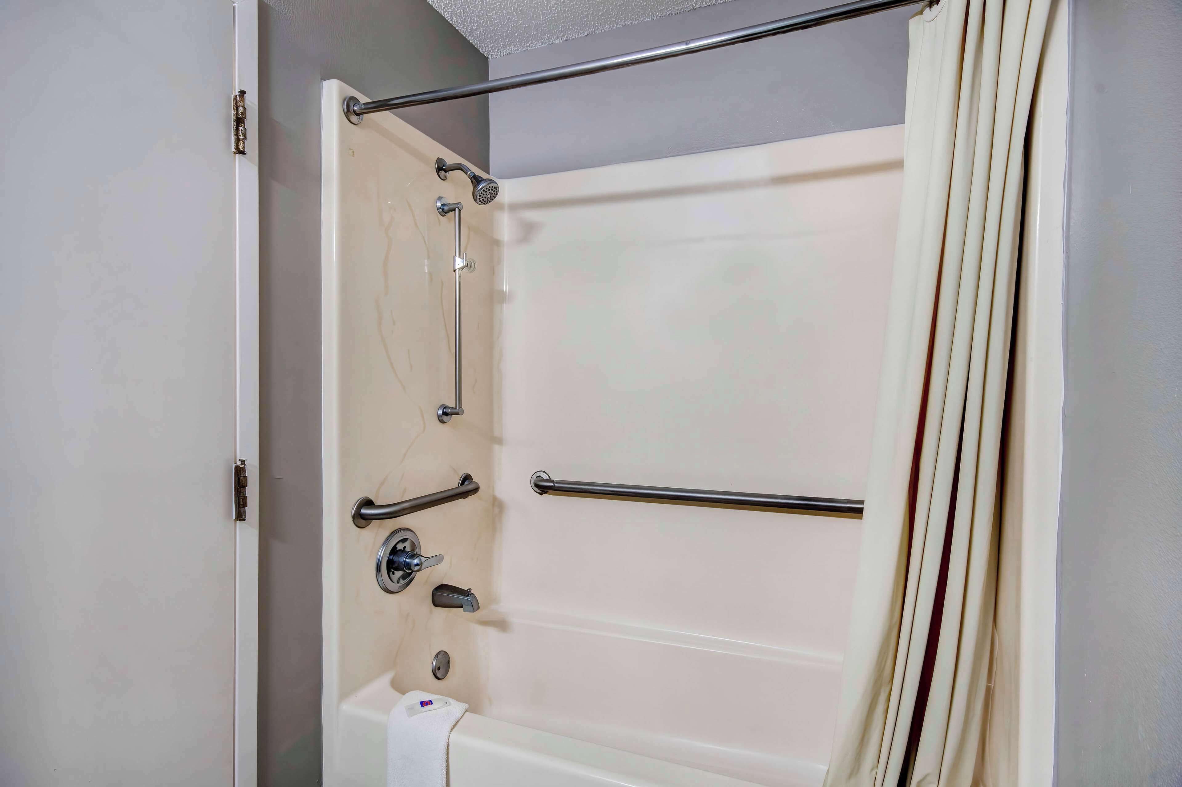A bathroom with a bathtub, grab bars, and a showerhead.